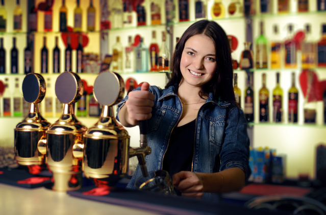 Bartender woman pours the beer into a glass