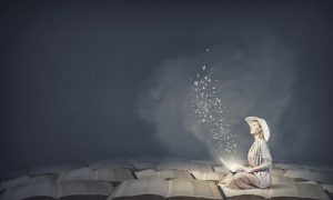 Woman in dress and hat sitting on books and working on laptop
