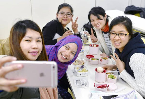 Những phụ nữ trẻ người Việt Nam và Philippines vui vẻ chụp ảnh chung trong một lớp học ở Osaka để chuẩn bị cho kỳ thi nhận chứng chỉ quốc gia về điều dưỡng tại Nhật Bản