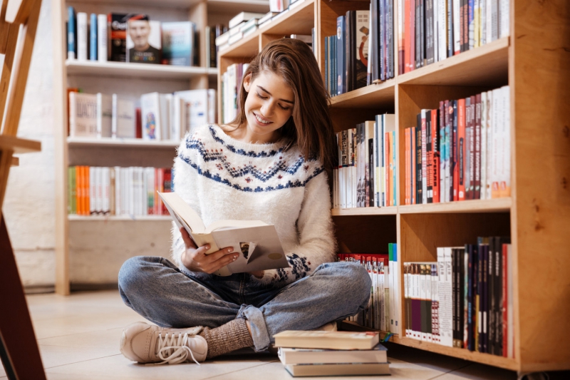 Pretty student reading book on library floor at the university