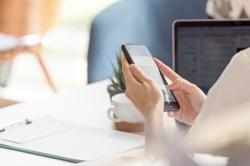 Female hand using smartphone while working at desk in office