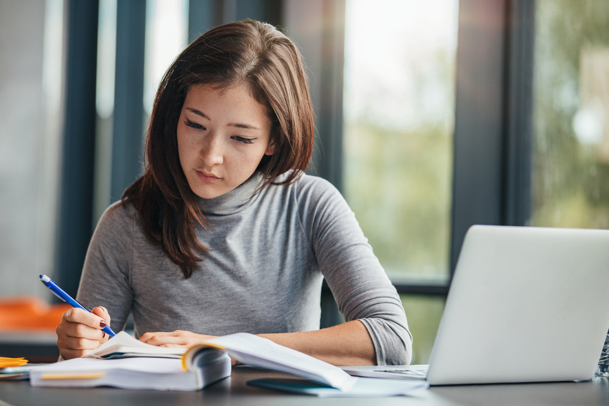 Shot of young woman taking down notes in diary. Female university student preparing note for the exam at library.