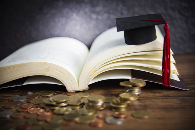 Scholarship for education concept with money coin on wooden with dark background and graduation cap on a open book