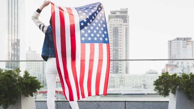 woman-standing-balcony-with-big-american-flag_23-2148157221