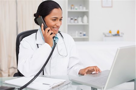 6109-06006911 © Masterfile Royalty-Free Model Release: Yes Property Release: Yes Smiling practitioner looking at her laptop while talking on the phone